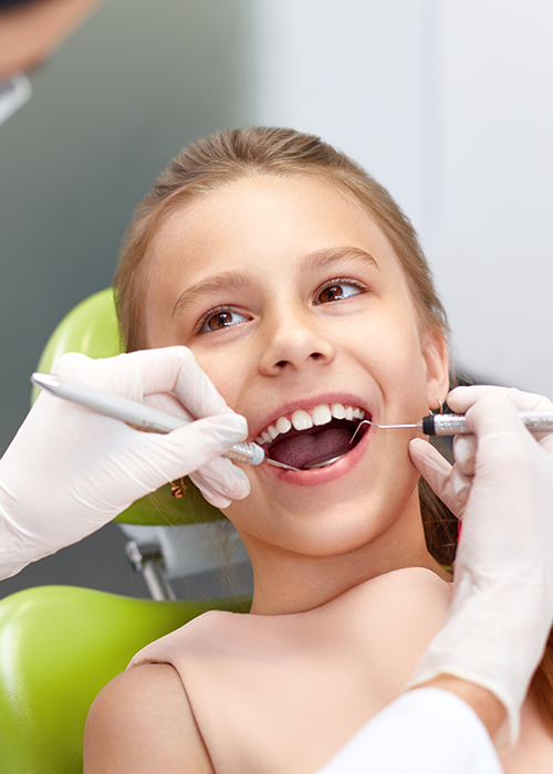 A kid with mouth open being examined by the dentist.